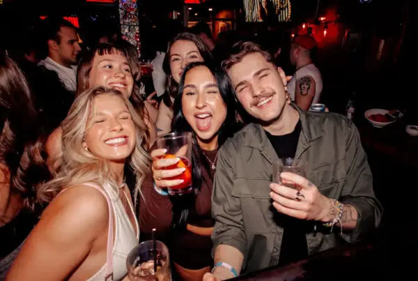 Group of friends smiling and raising cocktails at Warehouse during a lively night out.