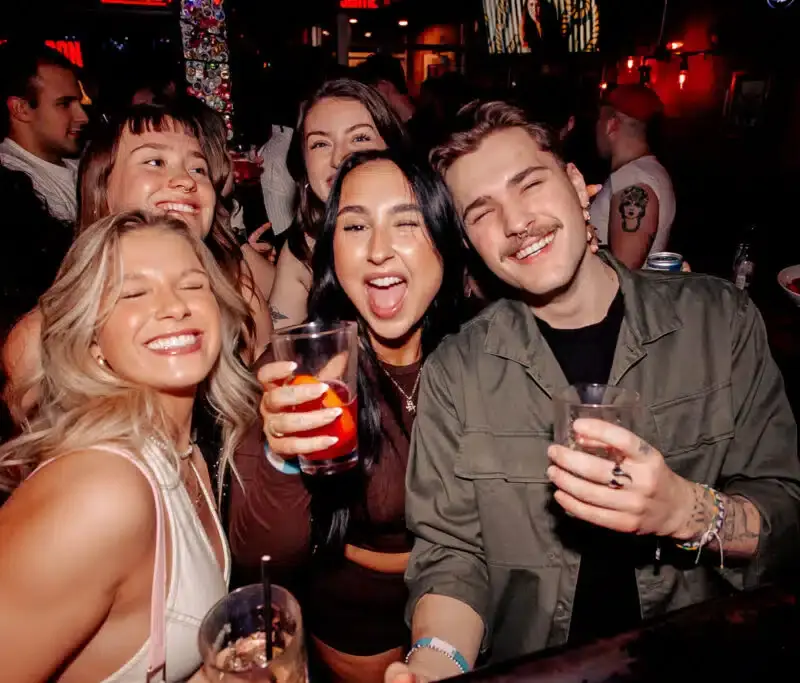 Group of friends smiling and raising cocktails at Warehouse during a lively night out.