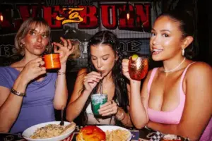 Three friends enjoying food and colorful cocktails at Warehouse during a lively bachelorette celebration.