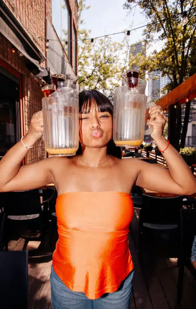 Woman holding two empty cocktail pitchers and posing inside Warehouse.