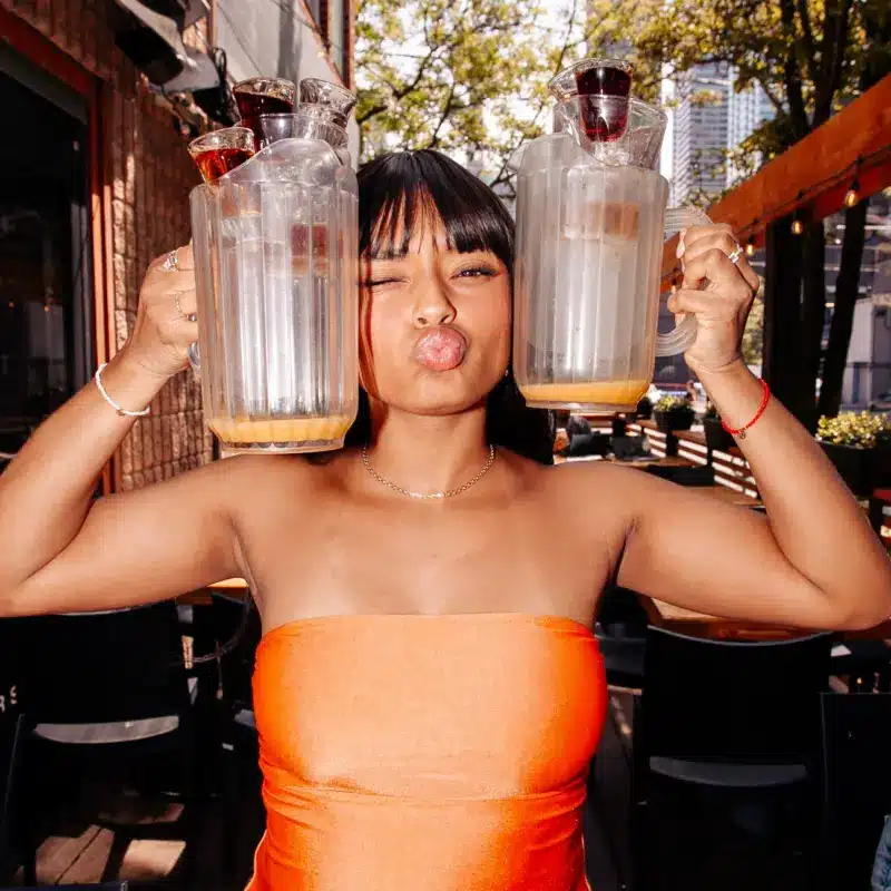 Woman holding two empty cocktail pitchers and posing inside Warehouse.
