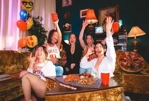 Friends celebrate with food and drinks at Warehouse Group, raising red cups around a table of shareable bites.