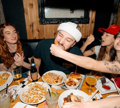 Friends sharing burgers, fries, and drinks at a Warehouse restaurant table.